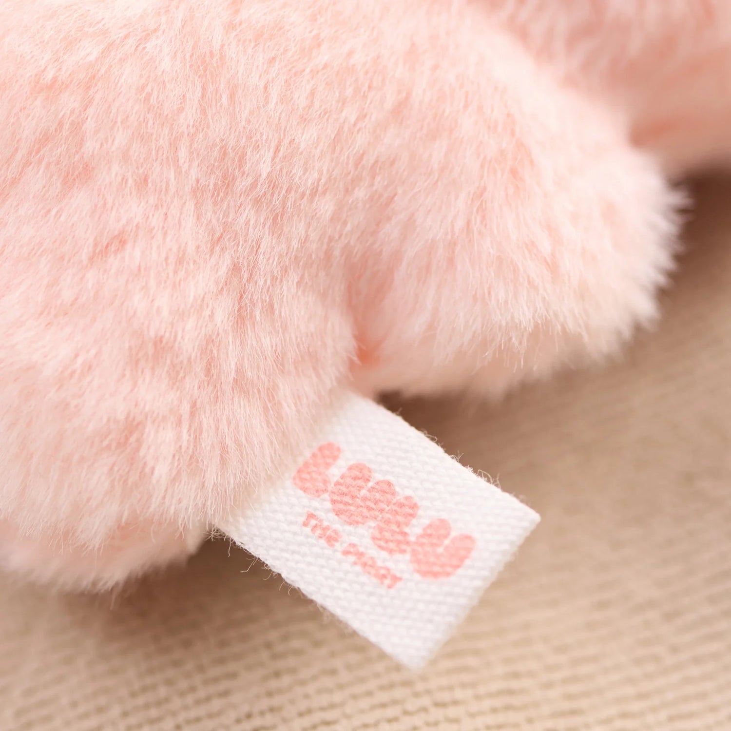 A close-up of a fluffy, light pink LuLu The Piggy - Mini LuLu Keychain plush with a white tag featuring "uwu" in pink letters.