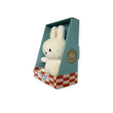 A cream-colored Mini Miffy Plush from the Miffy brand rests in a teal and orange checkered box labeled "The X Label," making it an ideal gift. The box highlights its "100% recycled filling." The toy's stitched black eyes and nose enhance its charm.