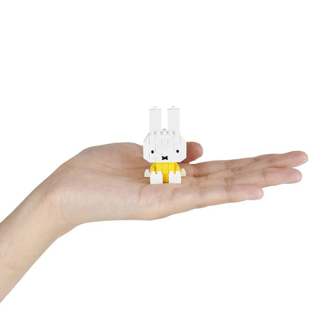 Hand holding a small assembled Nanoblock Miffy figure wearing yellow from Miffy Blind Bag Vol. 2 on white background