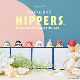 Adorable mini figures dressed in charming animal costumes adorn a tiled ledge, accompanied by characters with a sea-inspired theme. The backdrop showcases a blue and pink wall decorated with seashells and starfish. Text displays "Mofusand Hippers." Ideal for fans of the Mofusand Hippers Blind Box!