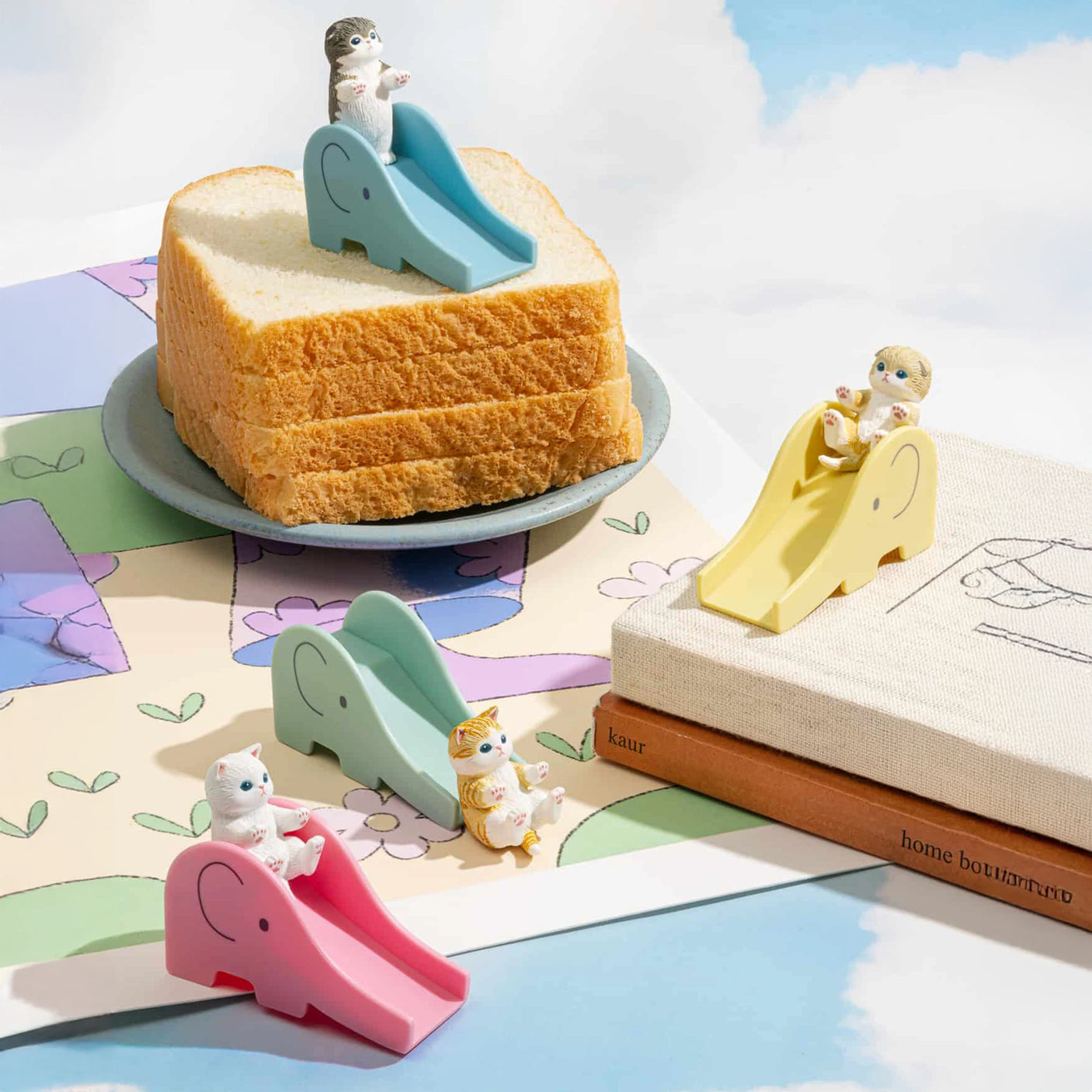 Three mini cat figures frolic on colorful slide toys around a slice of bread, set against a bright sky with clouds and drawings. Explore the whimsical world of Mofusand Blind Box - Cats on Slides!.