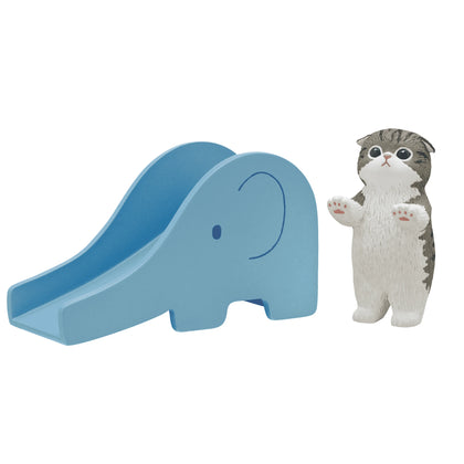 Cat figurine on blue slide, gray-and-white cat standing beside slide.