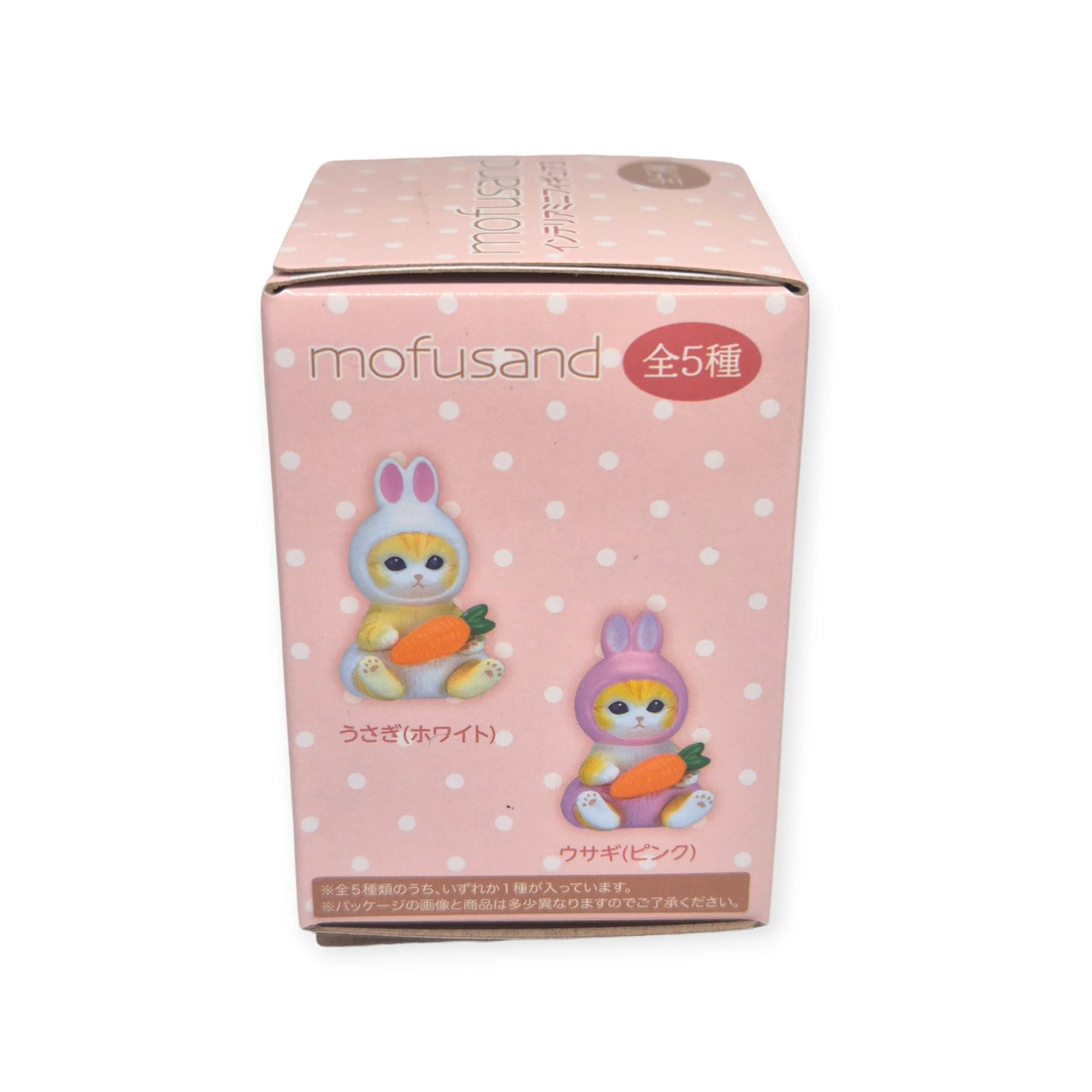 The Mofusand Mini Figure Blind Box - Vol 3 (Pink) features a whimsical design with polka dots, displaying illustrations of a cat dressed as a rabbit holding a carrot. The text indicates there are five collectible versions, each featuring adorable cat figures.