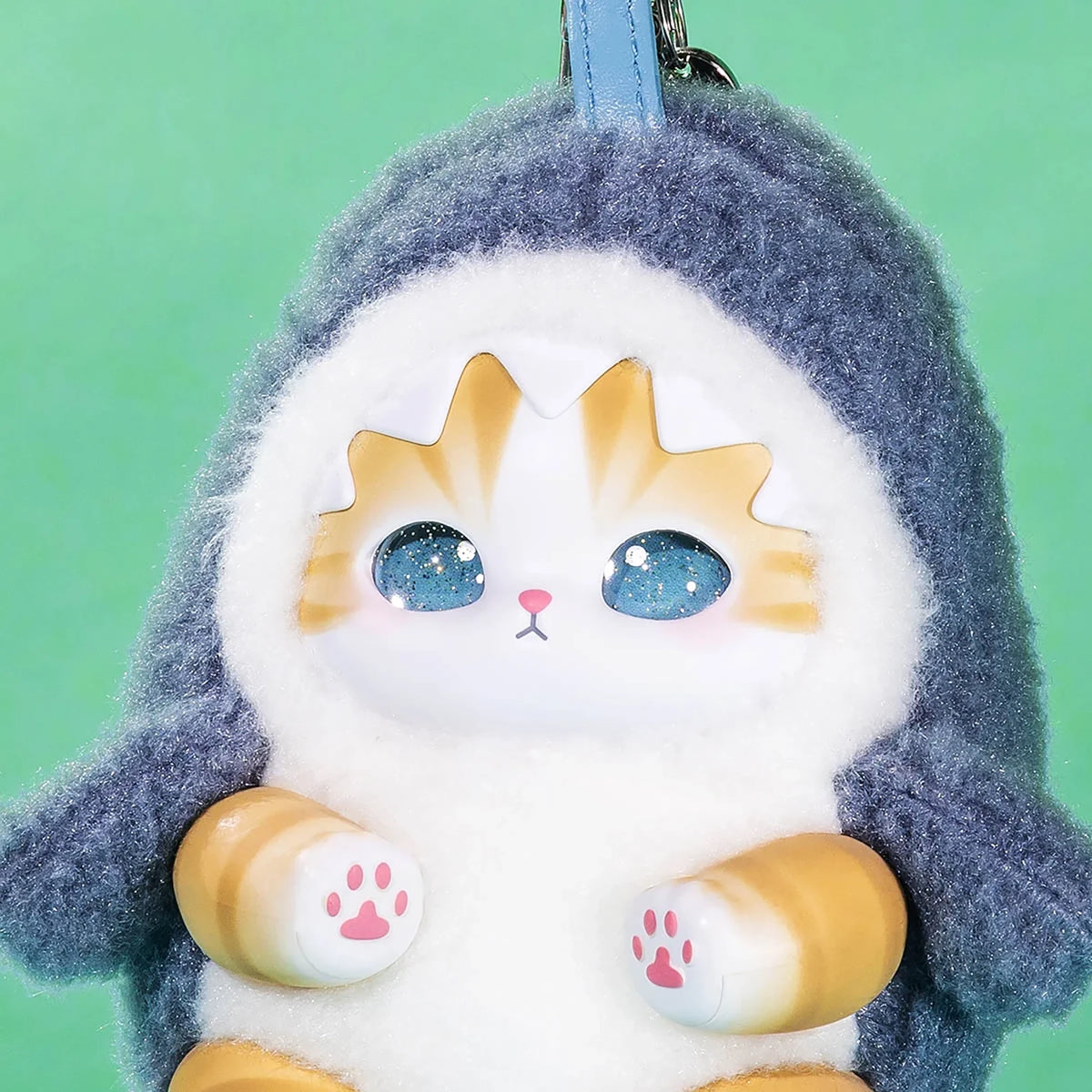 Close-up dark blue hooded kitten keychain plush with sparkling blue eyes and tan paw details