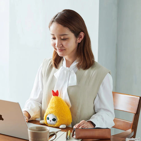 A woman sits at a table working on a laptop with the adorable Mofusand Posture Plush Buddy - Fried Shrimp by Mofusand resting on her lap.