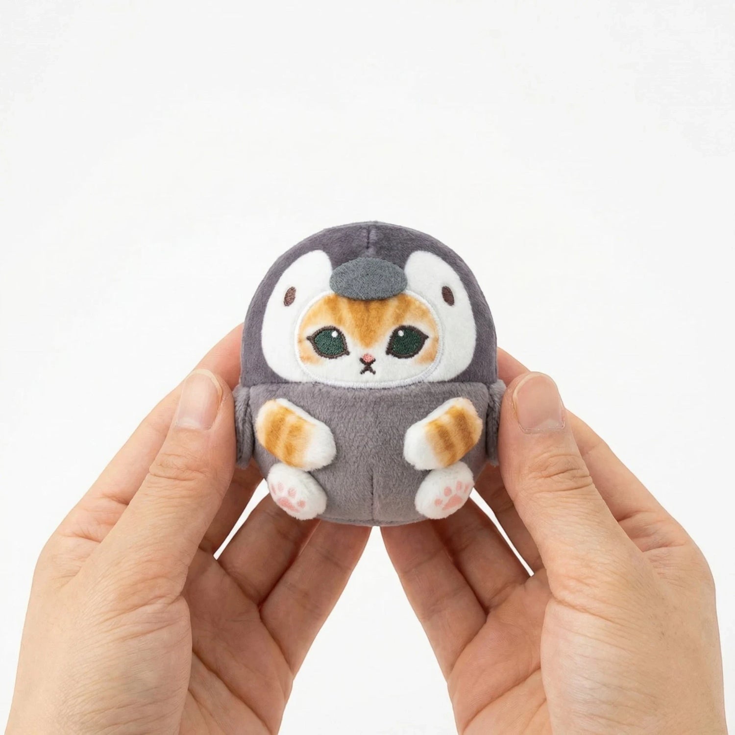 Gray penguin plush keychain held in hands, showing stitched face and flippers