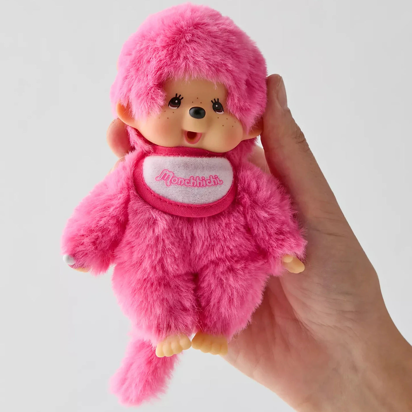 Monchhichi berry pink plush doll close-up, hood and logo scarf, held in hand