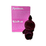 The Monchhichi plush toy, with its soft-touch finish, stands beside a purple box featuring English and Japanese text on its history and charm. It complements the intricate allure of the Monchhichi Flocked Figure Blind Box - Original Series by Monchhichi, creating a collector's delight.