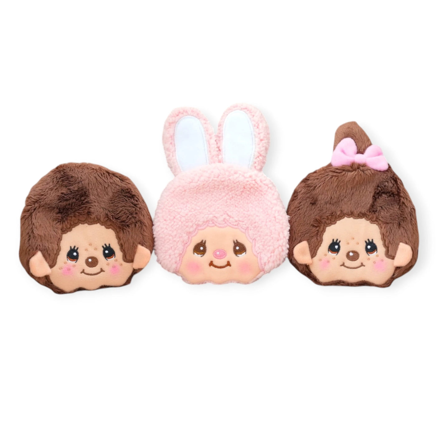 The Monchhichi Coin Pouch - Chimutan features three plush doll faces with rosy cheeks: two have brown hair, crafted from soft material, and one with a bow. The middle one is a charming Monchhichi Chimutan with pink hair and bunny ears.