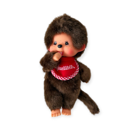 A Monchhichi Plush Doll - Twin Boy, by Monchhichi, stands upright with a red bib and thumb in mouth on a white background, evoking nostalgia and vintage vibes.