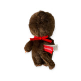 The Monchhichi Plush Doll - Twin Boy, a brown vintage-inspired toy with a nostalgic aura, features a red neck ribbon and displays its back. It has an attached tag on its side.