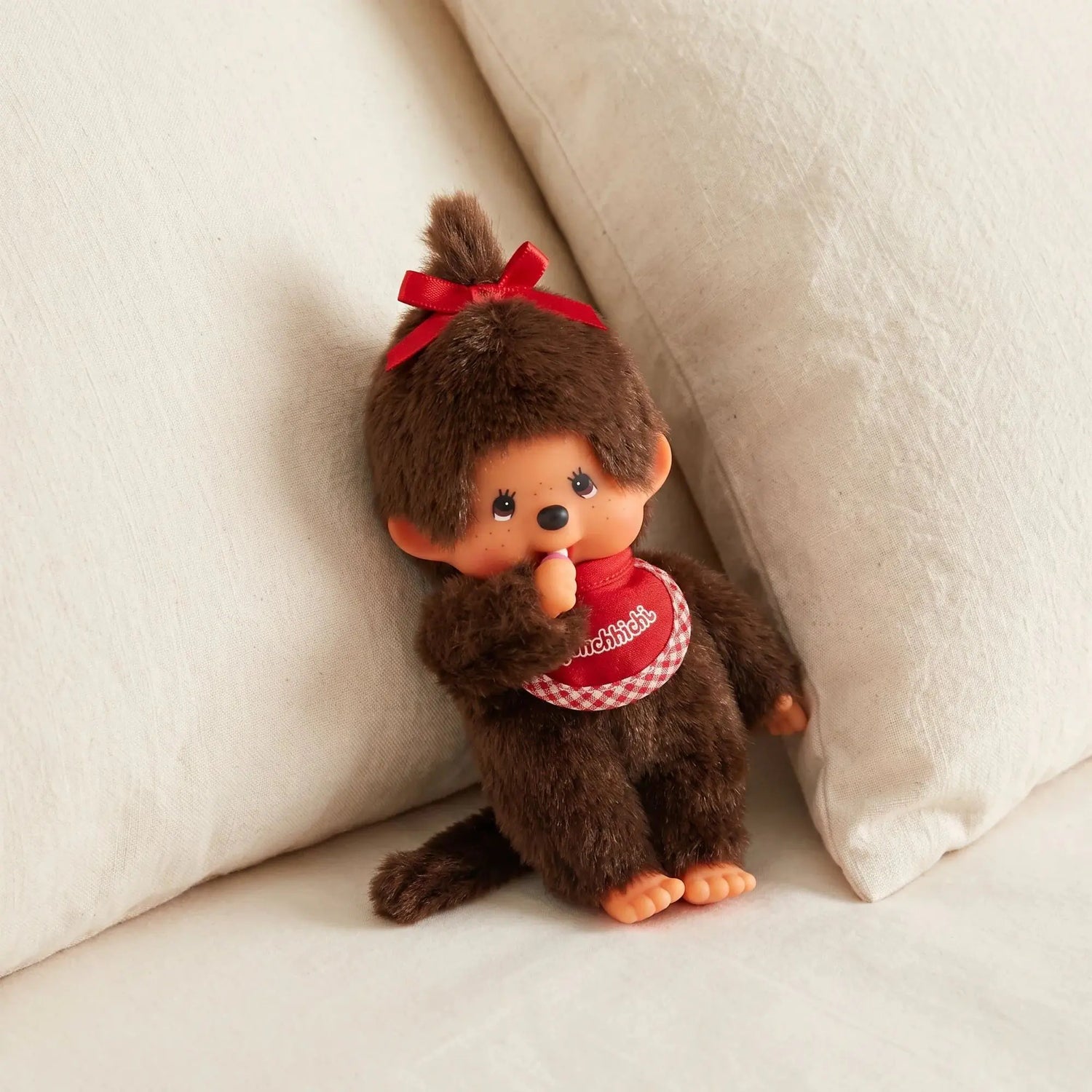 Monchhichi plush doll, brown fur, red bow and red checked dress, sitting