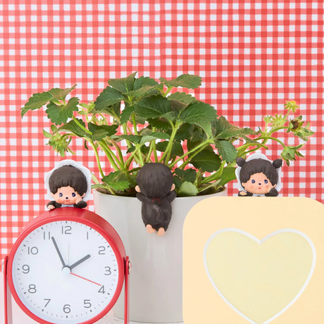 Three Monchhichi Hippers figures attached to a white plant pot and red clock on red gingham background