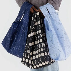 Person holding three patterned reusable bags with celestial designs.