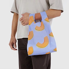 Person holding a blue reusable bag with an orange fruit pattern.