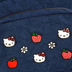 Dark blue fabric with embroidered designs of red apples, white flowers, and a character with a red bow.