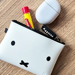 Small white pouch with a simple face design, alongside a tube of ChapStick and a white wireless earbud case on a wooden surface.