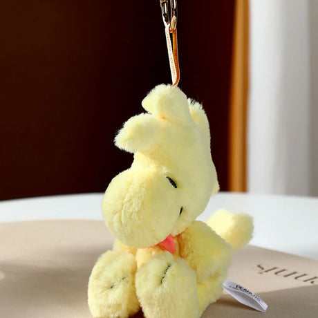 Soft yellow plush bird keychain with closed eyes and small orange beak hanging from tan strap