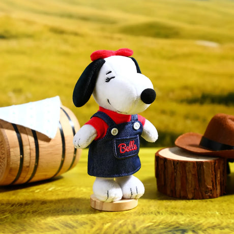 Snoopy plush keychain in dark denim overalls with red collar, on small wooden base