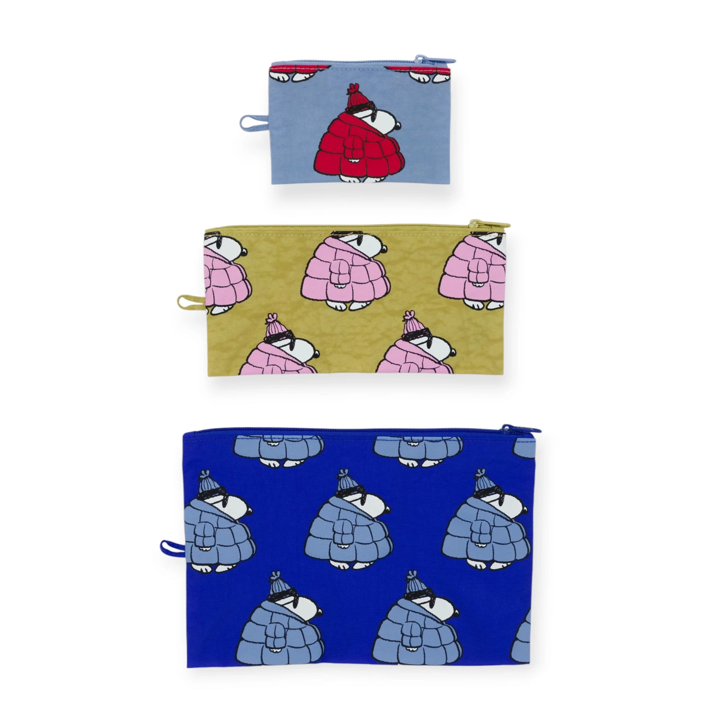 The Peanuts x Baggu Flat Pouch Set - Snoopy Puffer features three recycled nylon zippered pouches: small blue with red coat, medium olive with pink coat, and large blue with blue coat, adding playful charm to your accessories.