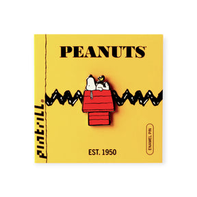Enamel pin of Snoopy and Woodstock relaxing on Snoopy’s red doghouse with black zigzag on yellow card backing