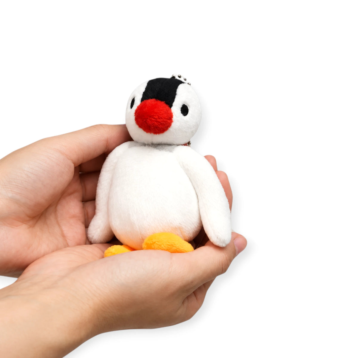 Plush penguin keychain held in hand, black head, red beak, white belly, orange feet