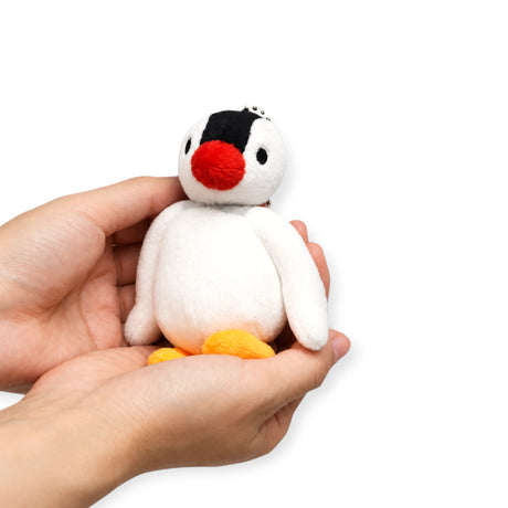 Plush penguin keychain held in hand, black head, red beak, white belly, orange feet