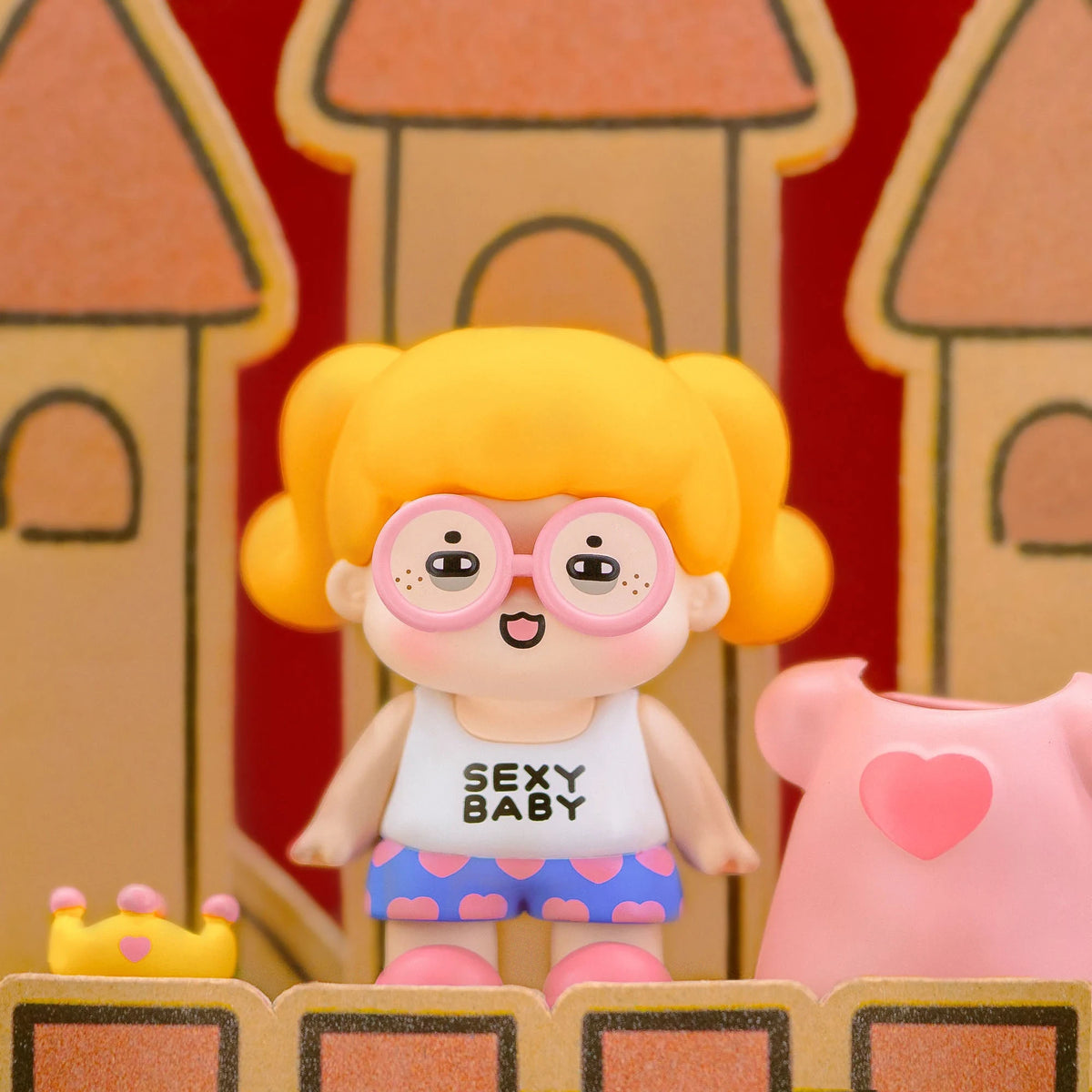 Blind-box figurine with orange hair, round glasses, pink top, and patterned shorts.
