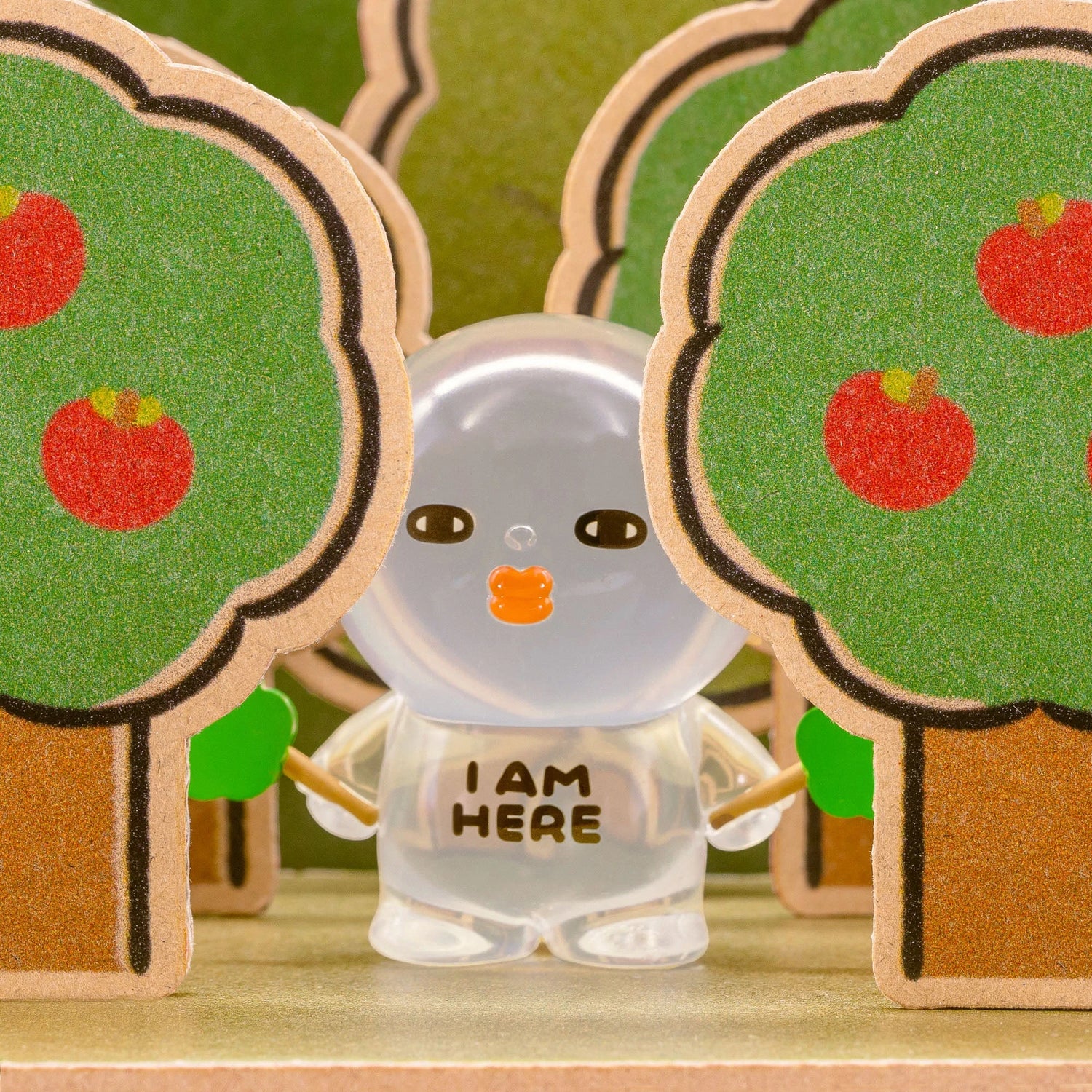 Clear-sleeve blind-box figurine standing between green hedges with orange emblem.