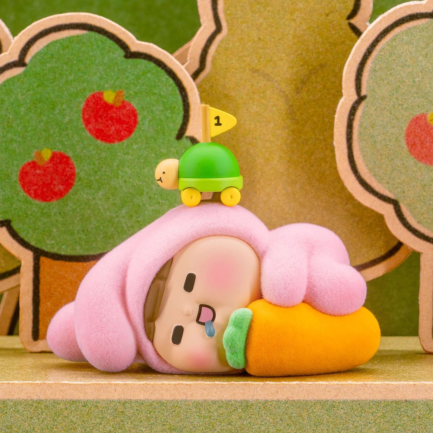 Pink earmuff blind-box figurine sleeping with orange-and-green face and small sign.
