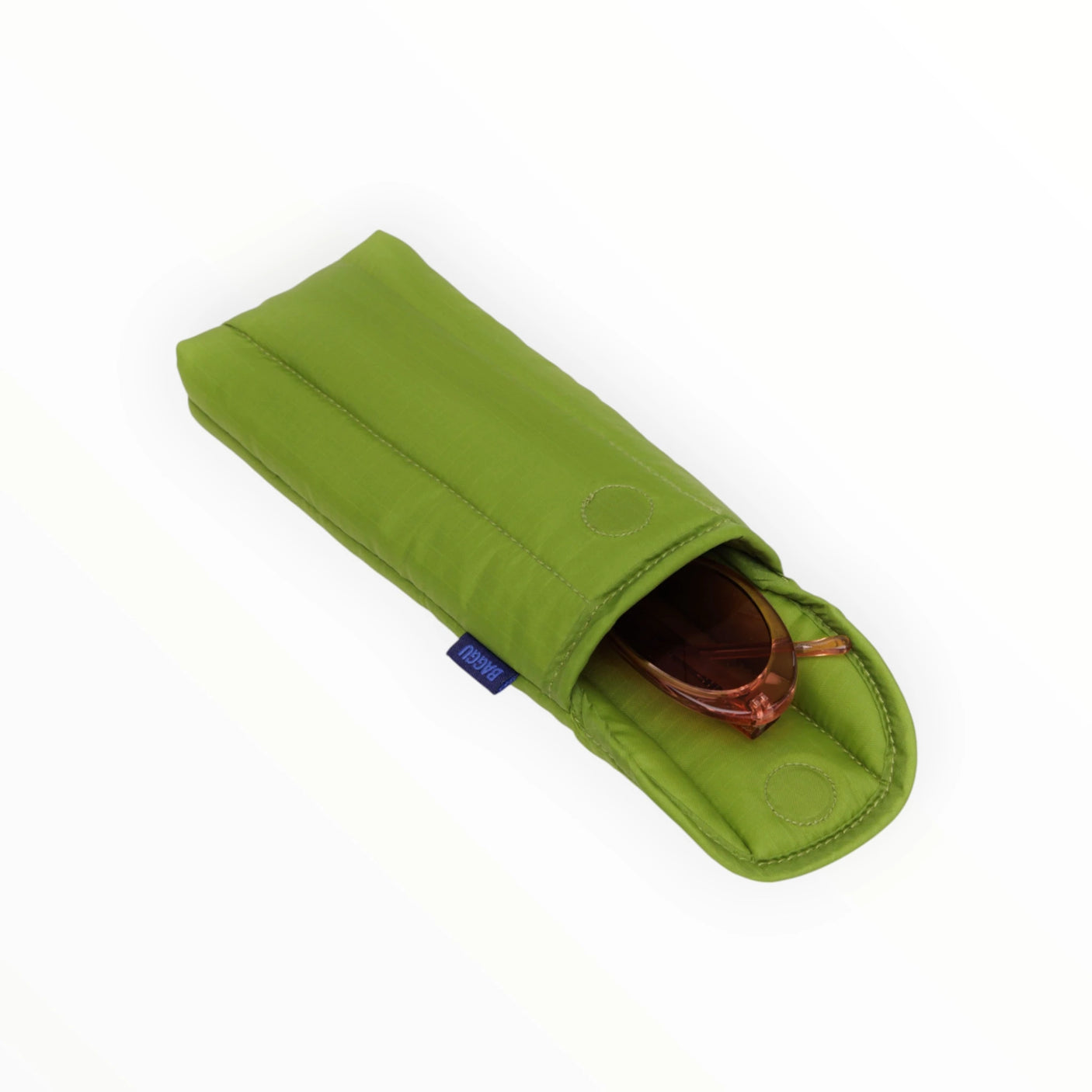 The Baggu Puffy Glasses Sleeve - Green Juice, made from recycled ripstop nylon with protective padding and a blue tag, holds a pair of sunglasses partially visible inside.