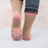 A person wearing the Pusheen Sock in a Mug Gift Set's cozy pink and beige socks adorned with paw print designs stands on a white surface, their jeans frayed and rolled up, next to the charming ceramic mug.