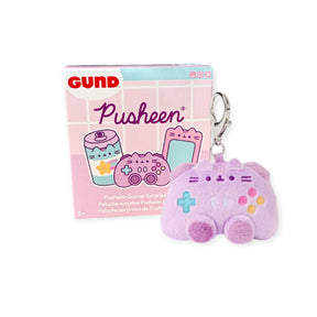 A pink Pusheen Gamer Series keychain shaped like a game controller sits next to its pastel-colored Pusheen Blind Box - Gamer Series by Pusheen.