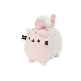 A cute, square plush toy from the Pusheen brand, known as the Pusheen Plush Mini - Roll Cake, features a white roll cake swirl pattern on the side and a small pink dinosaur sitting on top.