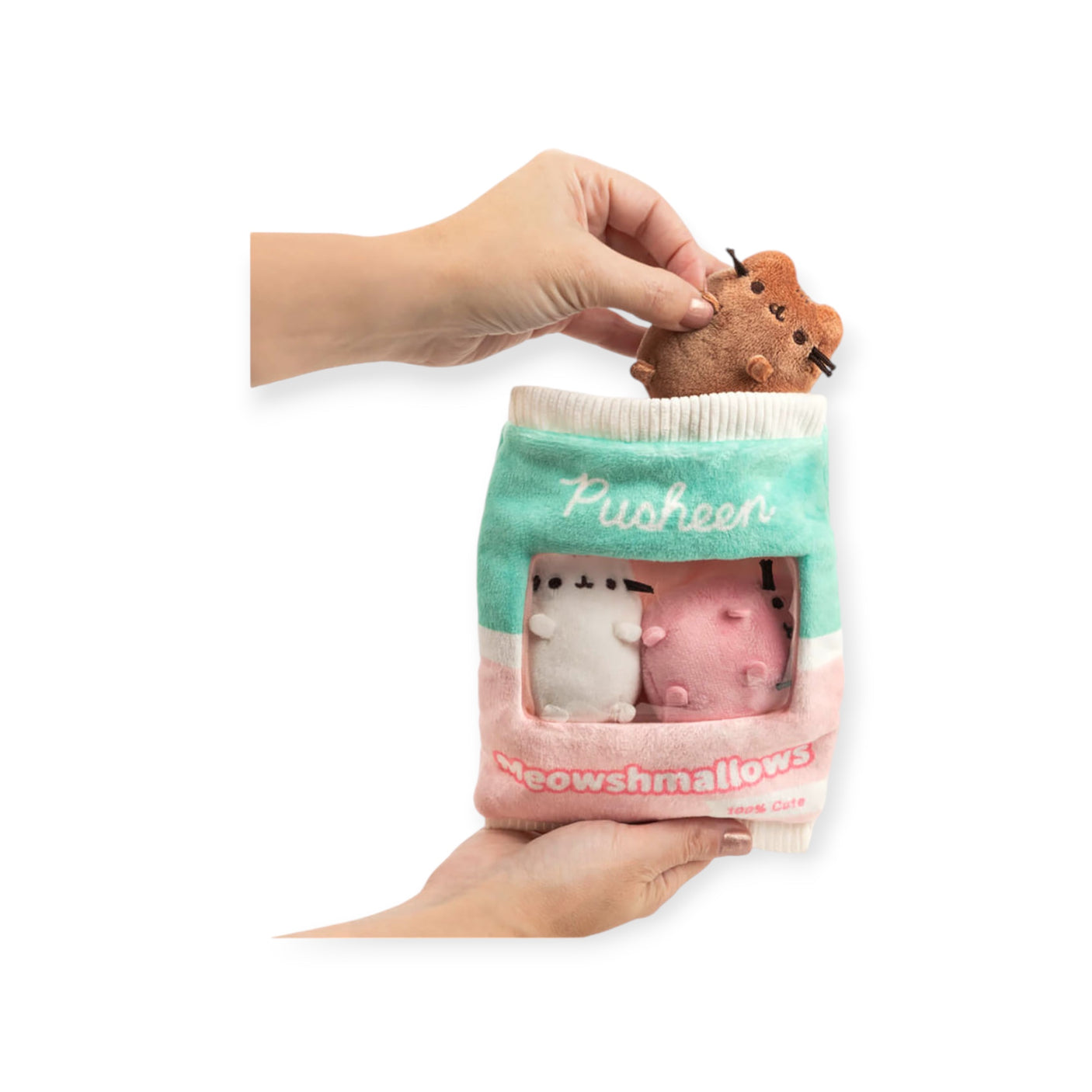 Two hands hold the whimsical Pusheen Meowshmallows Plush Gift Set, featuring delightful cat-themed designs that mimic a bag of treats. One hand places a small brown plush into the charming set, making it an adorable gift from Pusheen.