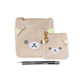 Two beige Rilakkuma Coin Pouch Keychain - 9cm featuring bear faces, crafted from synthetic leather—one larger than the other—sit next to a black pen with silver accents. Perfect for storing small essentials or attaching to a keychain, they add a playful touch.