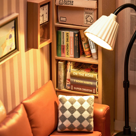 Create your own cozy miniature lounge room with the Rolife Cozy Living Lounge - DIY Plastic Mini House, featuring a brown leather sofa, checkered pillow, and floor lamp. The bookshelves are filled with books and a clock, highlighting your interior design skills.