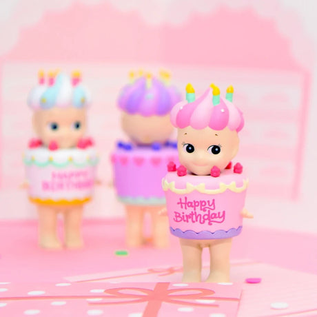Birthday mini figurine in pink hat and cupcake dress, with other figures behind