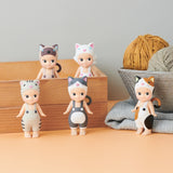 Five figurines from the Sonny Angel Cat Life Series by Sonny Angel are displayed on a surface. Three stand in front, while two are perched on a wooden box. Nearby is a bowl with yarn and folded fabric, perfectly capturing the charm of this limited edition collection.