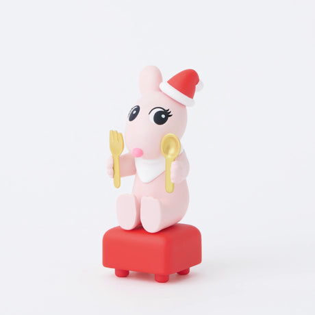 A pink cartoon rabbit, similar to a Sonny Angel, perches on a red stool adorned with a Santa hat. It clutches a gold fork and spoon, eagerly anticipating the Christmas dinner surprise tucked inside its very own Sonny Angel Christmas Dinner - Blind Box.