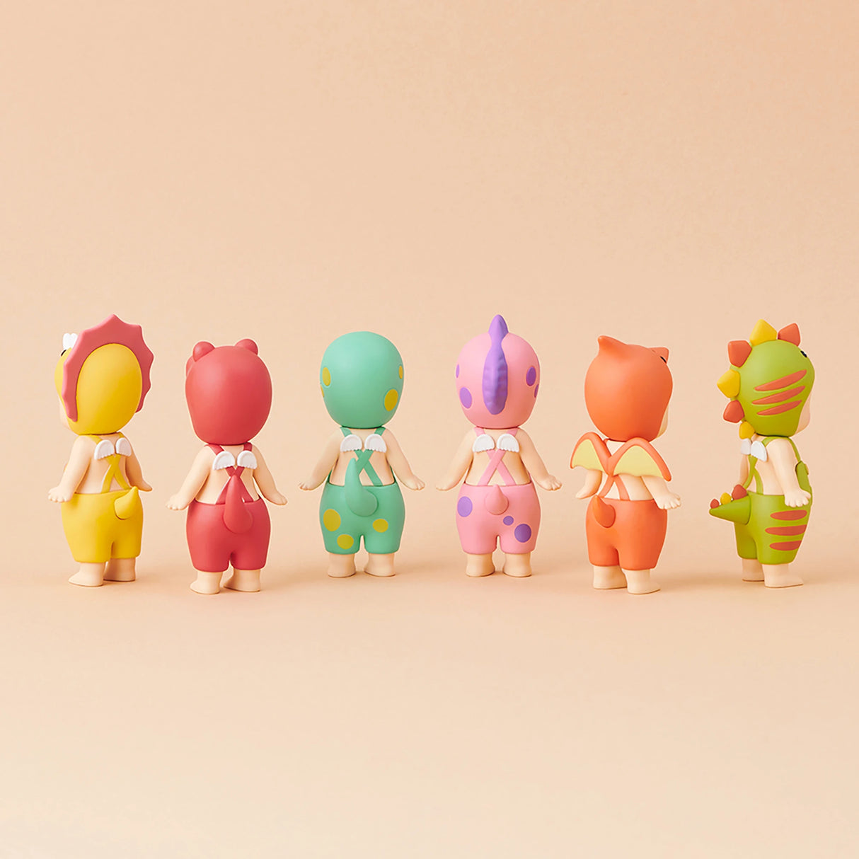 Six Sonny Angel figurines from the limited edition Dinosaur Series stand in a row on a beige background, their backs to us. Featuring colorful, animal-themed costumes, these prehistoric pals by Sonny Angel capture imaginations with delightful charm and vintage flair.