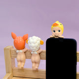 Three small figurines from the Sonny Angel Hippers Blind Box - Animals series, each wearing animal-themed hats, are perched on a wooden frame. The Sonny Angel figure on the right skillfully balances on the edge of a smartphone using its reusable adhesive.