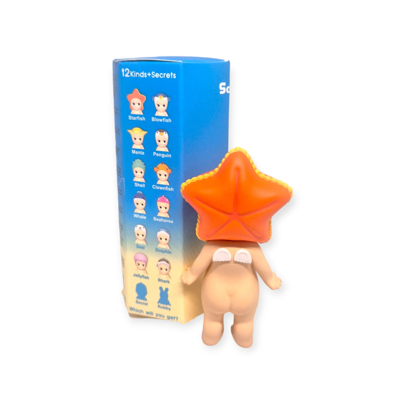 The toy figure sporting a large starfish hat is positioned beside the Sonny Angel Marine Series box, a collector's delight showcasing an array of fish and sea creatures. This box offers the excitement of 12 different kinds, each promising the surprise of revealing a mystery figure.