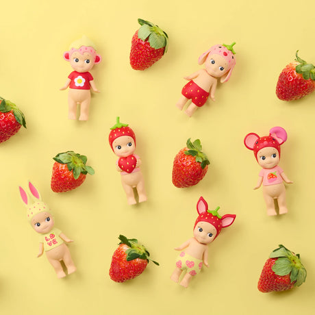 Seven small figurines wearing strawberry and animal-themed headwear arranged with fresh strawberries on yellow background