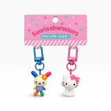 Two character keychain charms on a card: multicolor figure with blue lock, white cat with pink bow