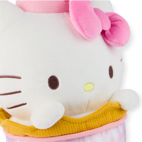 A Hello Kitty plush from the "Ice Cream Sundae" collection peeks from a cozy yellow and pink checkered blanket, its white face adorned with a cute pink bow, epitomizing the charm of Sanrio merchandise.