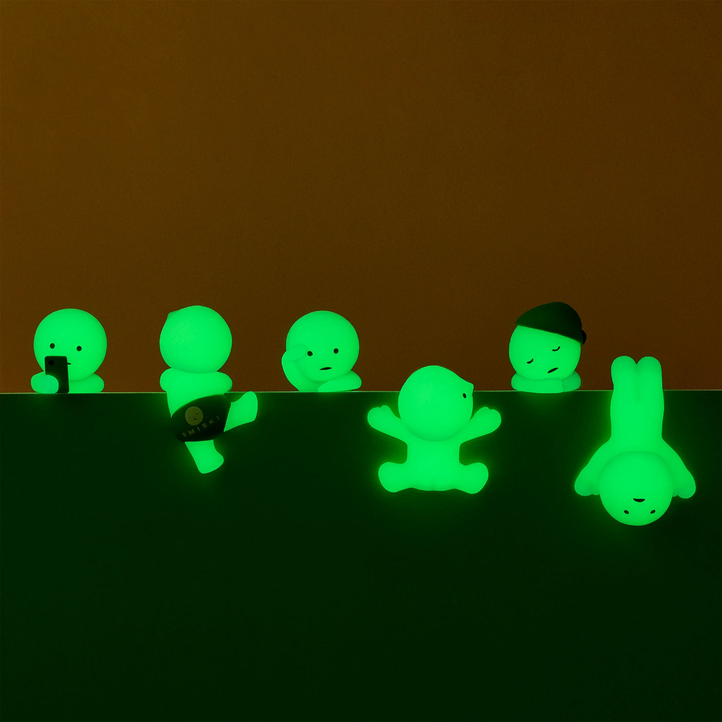 Glowing green figures from the Smiski Hippers Blind Box, by Smiski, display a range of poses and expressions on a dark backdrop.