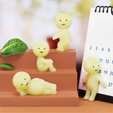 Four small, yellow, expressionless figurines from the Smiski Series 1 - Blind Box by Smiski are arranged on steps next to a calendar, with a green leaf nearby. These charming characters have a mysterious allure, as some even glow-in-the-dark.