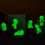 Glowing green cartoon figures from the Smiski Sunday Series - Blind Box pose on and around blocks, with a glow-in-the-dark calendar set to March 2025 in the background, complemented by a quirky cactus on the side.