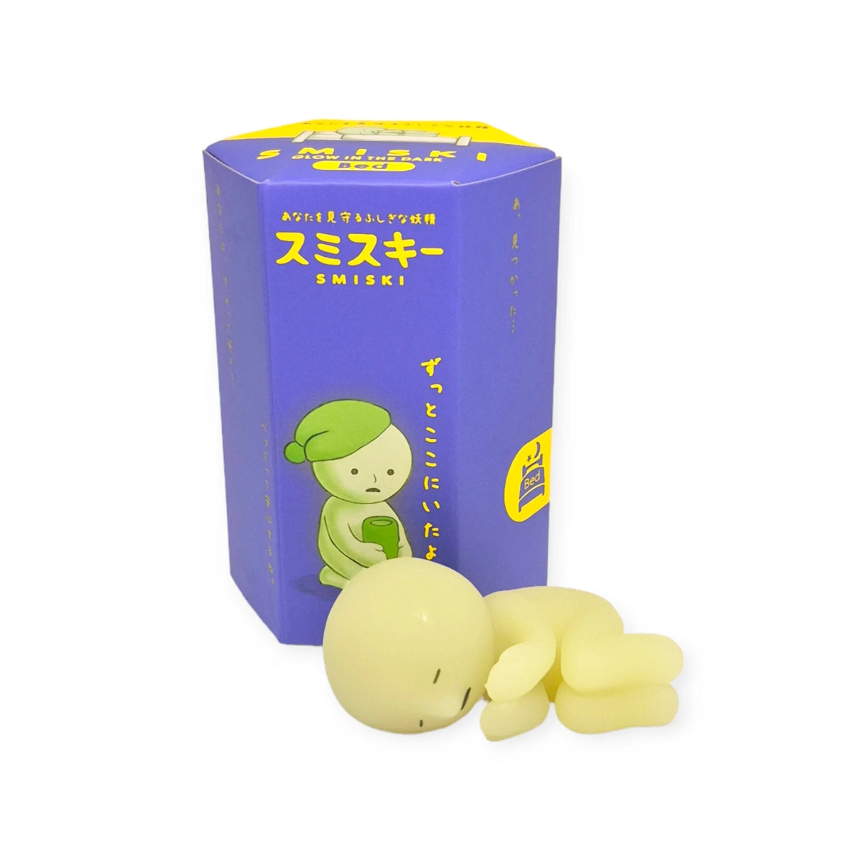 A photo featuring a green Smiski figure from the Bed Series, next to its Blind Box packaging. The figure is capable of glowing and is depicted in a unique sleeping or resting pose.